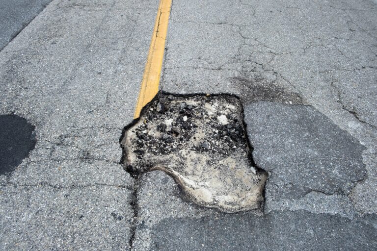 Damaged asphalt road with deep pothole on american highway surface. Ruined roadway in urgent need of repair